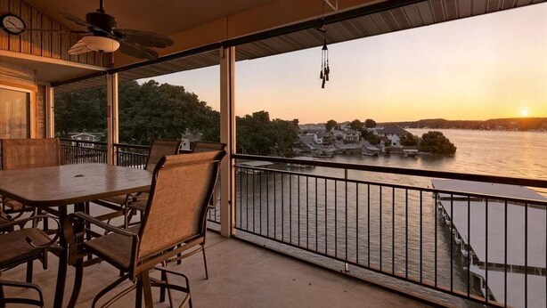 Ein Balkon mit Tisch und Stühlen, der auf einen Fluss mit Gebäuden und Booten im Abendrot blickt.