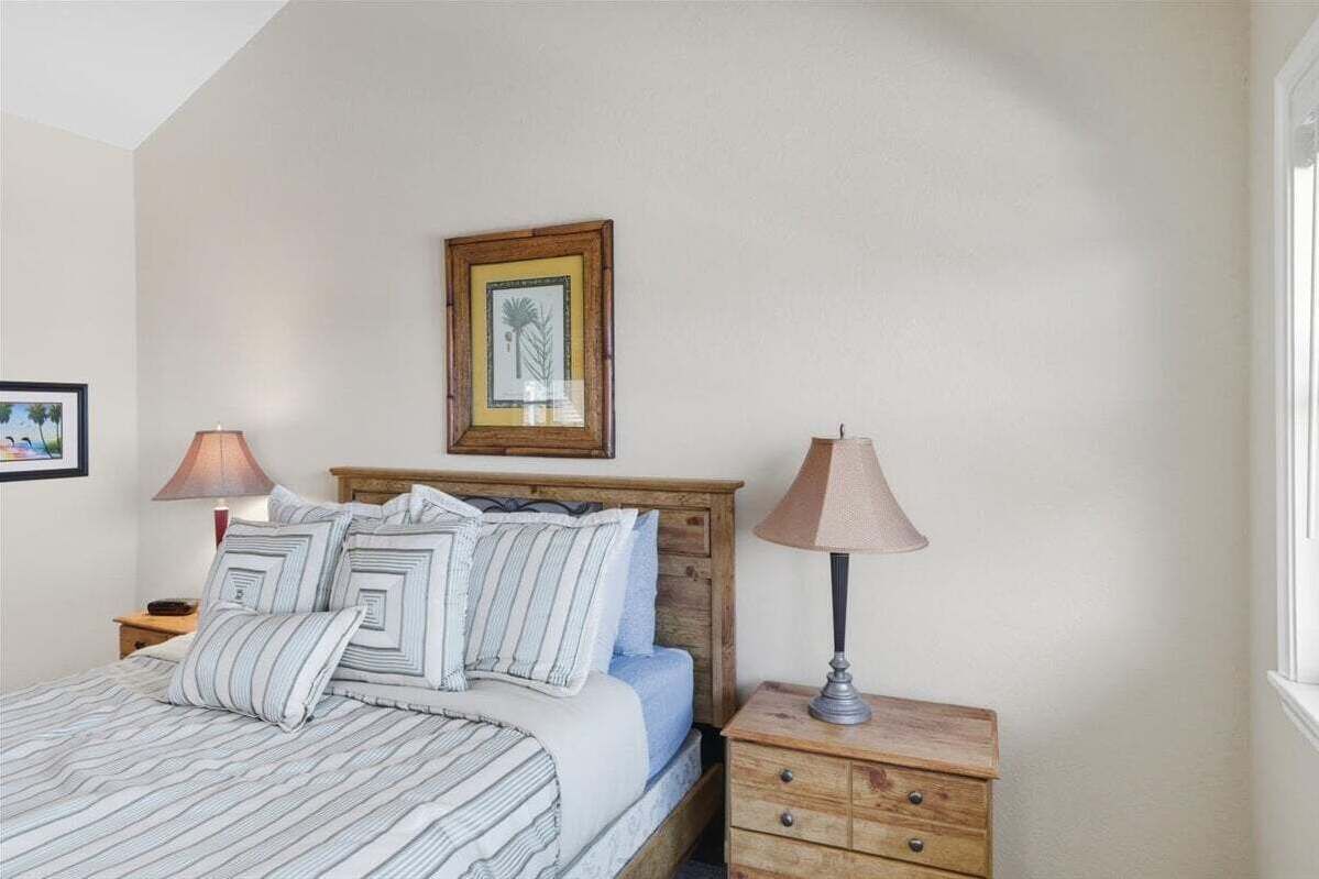 A bedroom with a bed, two bedside tables, a nightstand, a framed picture on the wall, and a window.