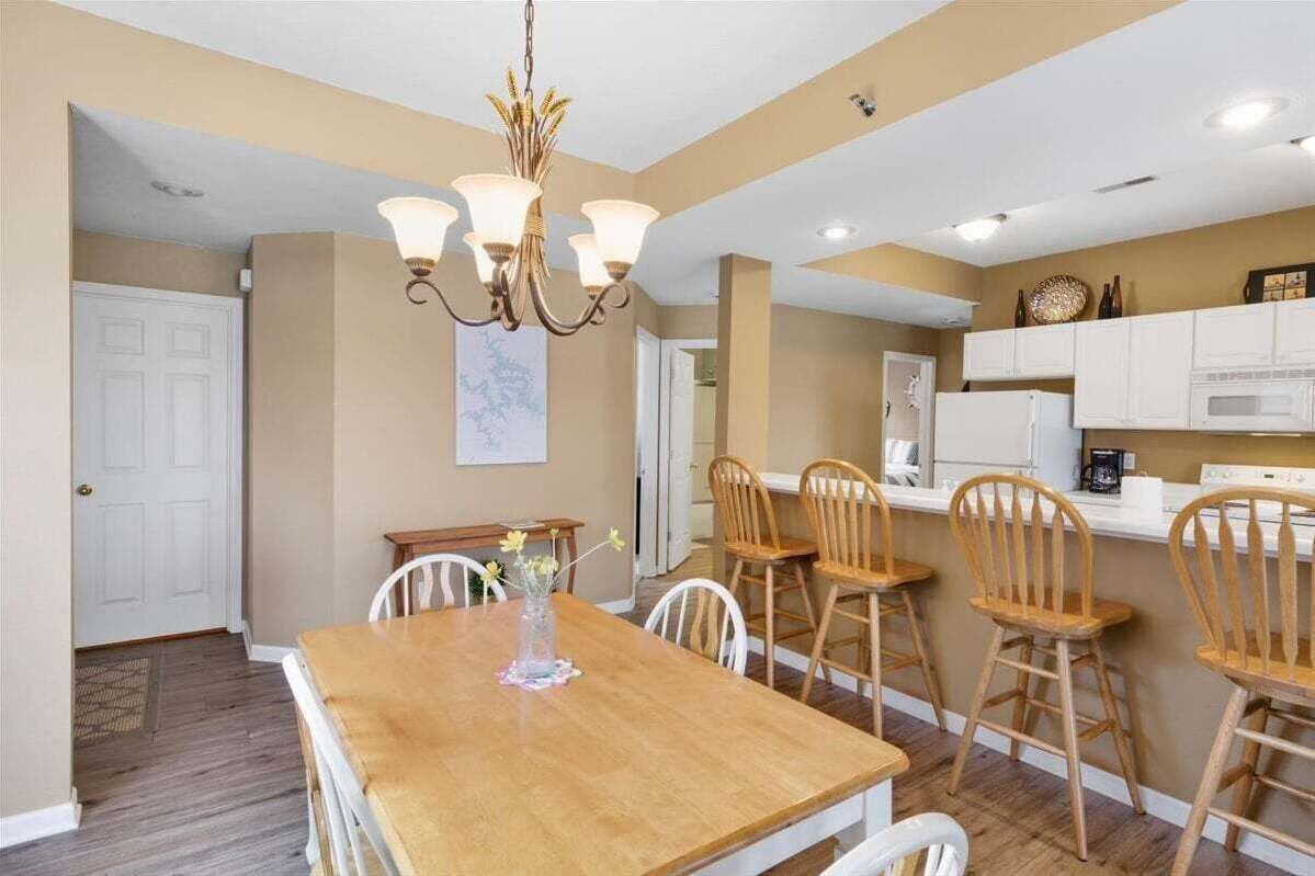 A dining area with a wooden table and chairs, a chandelier, and white cabinets in the background.
