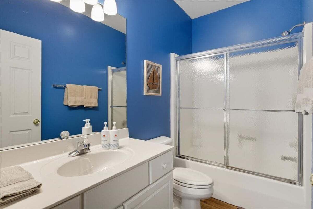 Une salle de bain avec un mur bleu, un lavabo blanc et une douche fermée par une paroi de verre.