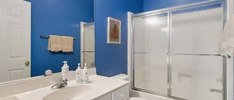 Une salle de bain avec un mur bleu, un lavabo blanc et une douche fermée par une paroi de verre.