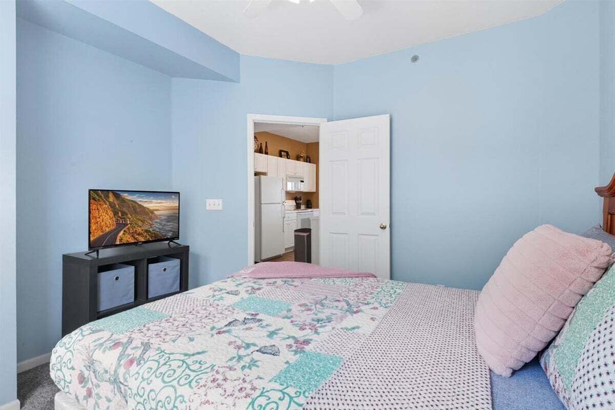 Quarto com cama, televisão em móvel, porta para banheiro e vista da cozinha.