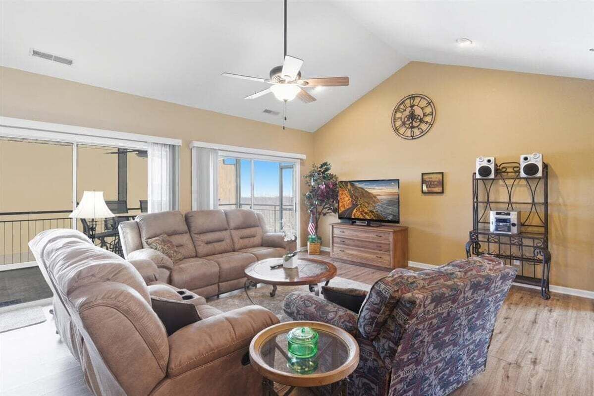 A spacious living room with a ceiling fan, a large window, a television, and a speaker system.