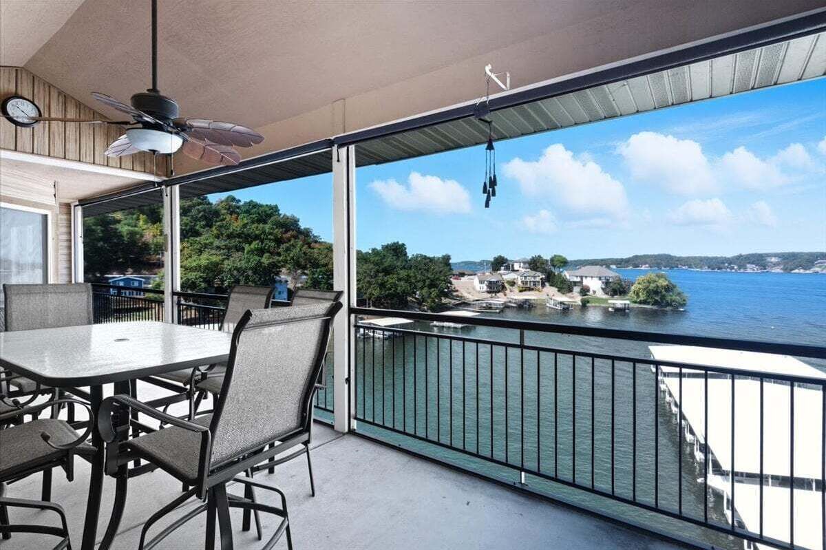 Un balcón con mesa y sillas, con vista a una masa de agua y una costa distante con edificios.
