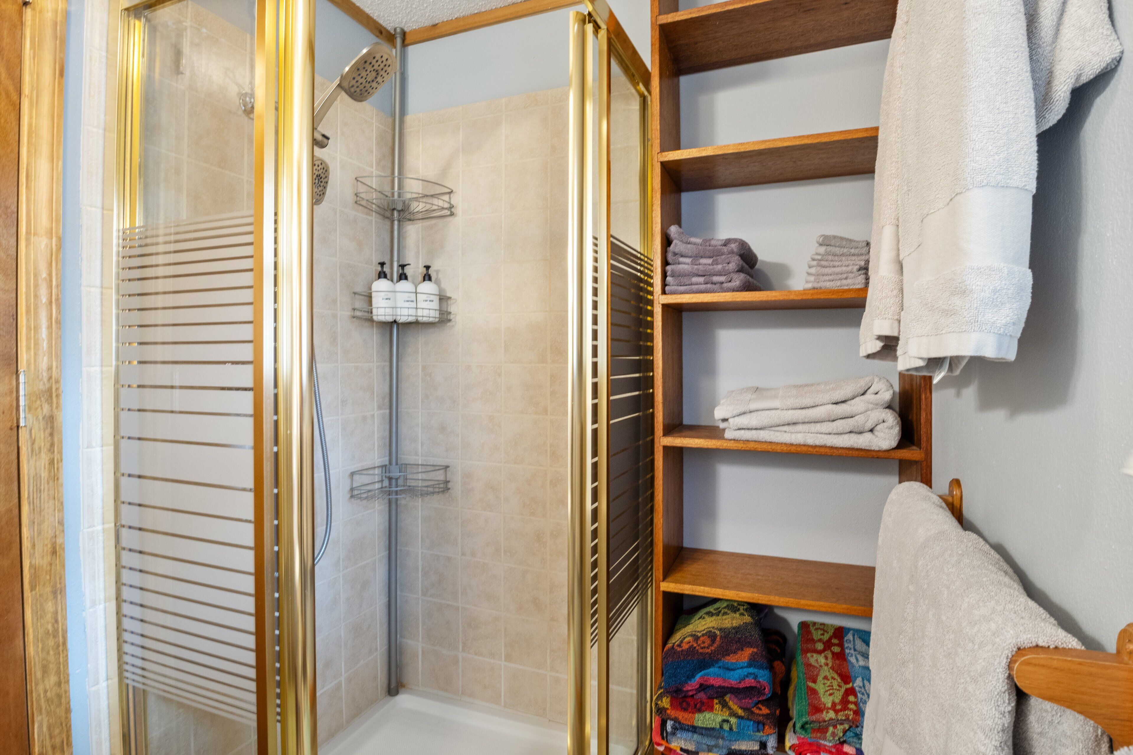 A bathroom with a glass-enclosed shower, shelves with towels, and toiletries.
