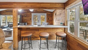 A cozy cabin interior with a wooden interior, a kitchen area with stools, and large windows offering views of the outdoors. - Stunning Lake View On A Nice & Quiet Relaxing Home (Climax Springs)