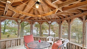 A covered outdoor area with a wooden ceiling, a round table with chairs, and large windows offering a view of trees and buildings. - Stunning Lake View On A Nice & Quiet Relaxing Home (Climax Springs)