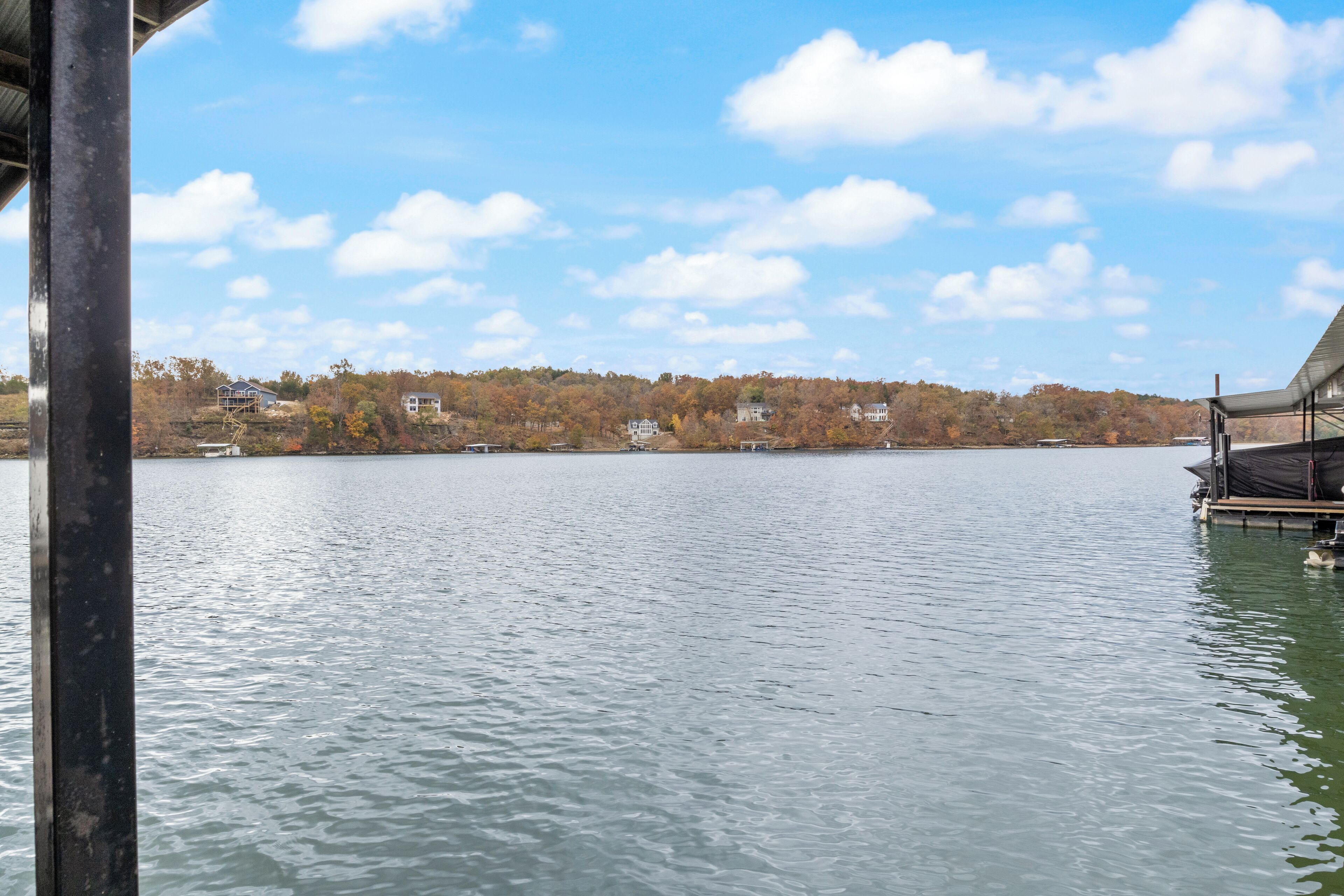 Un lago tranquilo con un muelle y casas al fondo.
