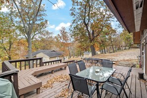 An outdoor deck with a glass table and chairs, surrounded by wooden benches and a railing. - Stunning Lake View On A Nice & Quiet Relaxing Home (Climax Springs)