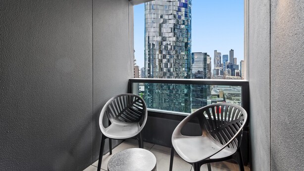 A balcony with two modern chairs and a small round table, overlooking a cityscape with tall buildings. - 2-bed Inner-city Pad With Pool, (Melbourne)