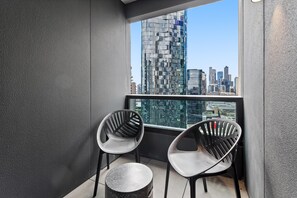 Ein Balkon mit zwei modernen Stühlen und einem kleinen runden Tisch, mit Blick auf eine Skyline aus hohen Gebäuden.