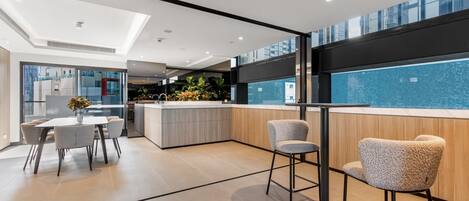 A modern kitchen with a central island, a dining area with a table and chairs, and a view of a pool through large windows.