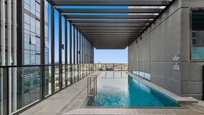A modern indoor pool with a glass enclosure, a metal ladder, and a view of the cityscape. - 2-bed Inner-city Pad With Pool, (Melbourne)