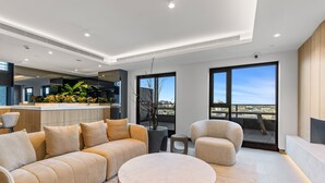 A modern living room with a sofa, a round coffee table, and a chair. There is a balcony with a view of the city. - 2-bed Inner-city Pad With Pool, (Melbourne)