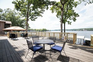 Une terrasse en bois avec une table ronde et des chaises, donnant sur une étendue d’eau.