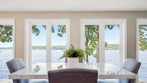 Een eetgedeelte met een glazen tafel en twee grijze gestoffeerde stoelen, met uitzicht op een waterpartij en groen.