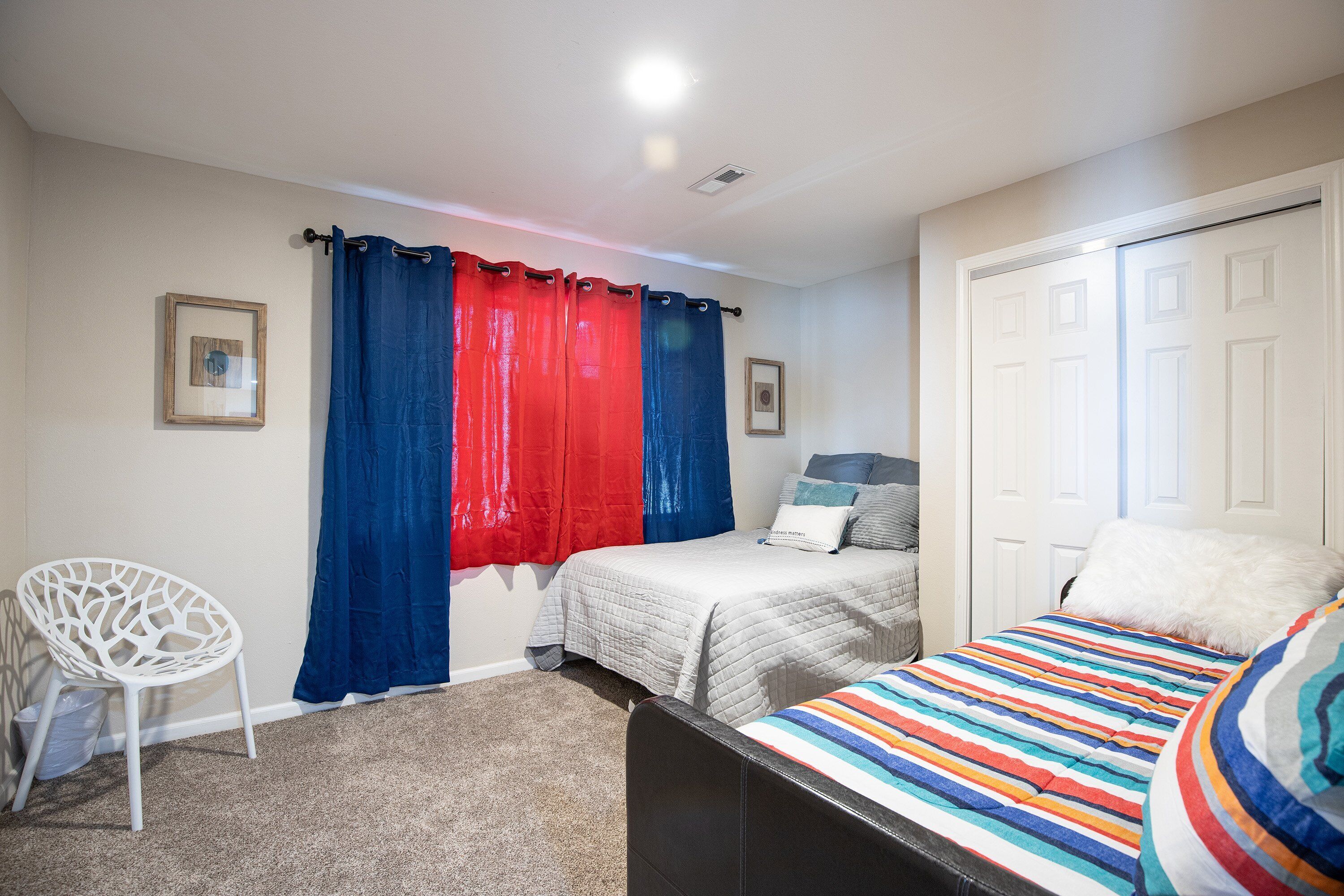 A bedroom with a bed, a chair, a wardrobe, and a window with curtains.
