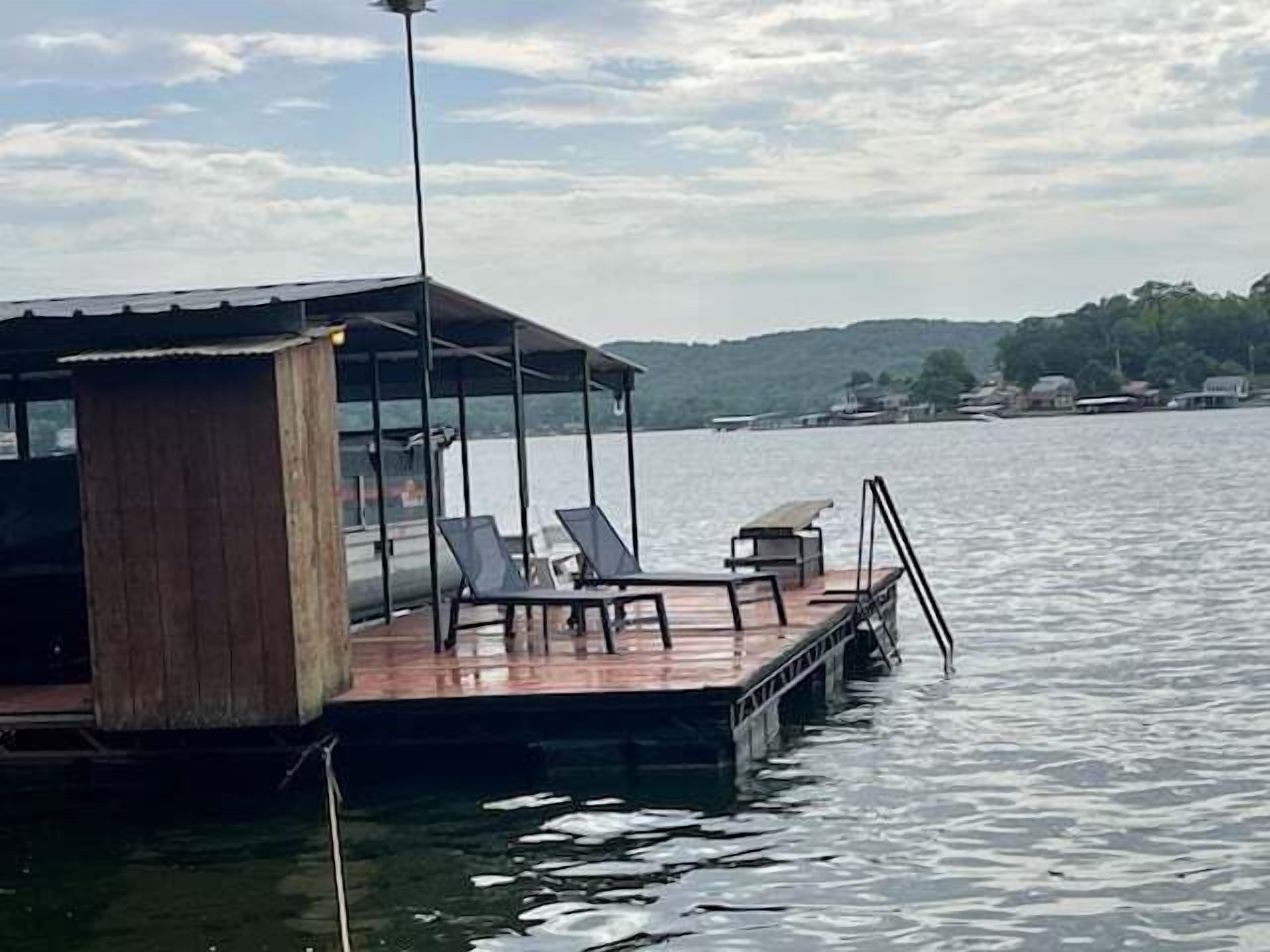 Un muelle con zona de estar cubierta, una estructura de madera y vista al agua y a la costa distante.