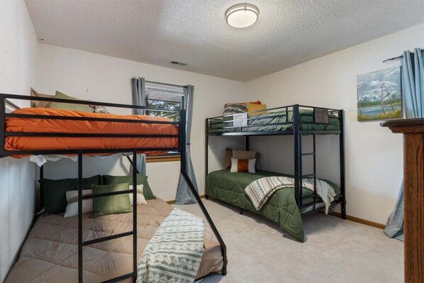 A dormitory room with bunk beds, a window with curtains, and a painting on the wall.
