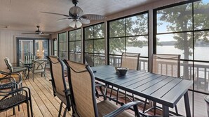 A covered outdoor dining area with a table and chairs, large windows, and a view of a lake. - Quiet Cove, Private Dock, Fishing, Swimming, Boat Slip & Kayaks (Camdenton)