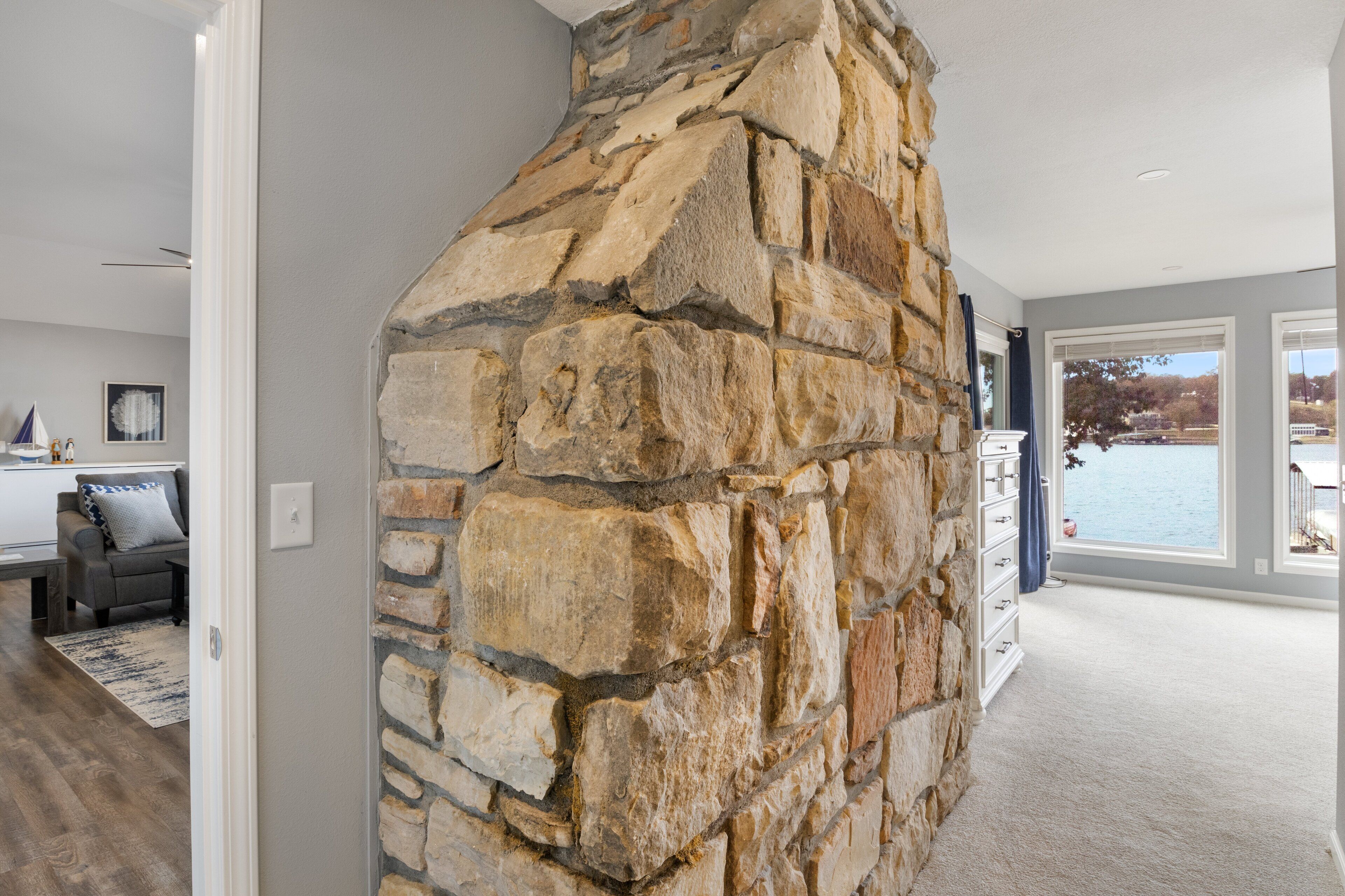 A stone fireplace in a modern living room with a view of a lake.