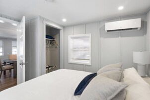 Un dormitorio con cama, armario, ventana con persianas, aire acondicionado y una lámpara.