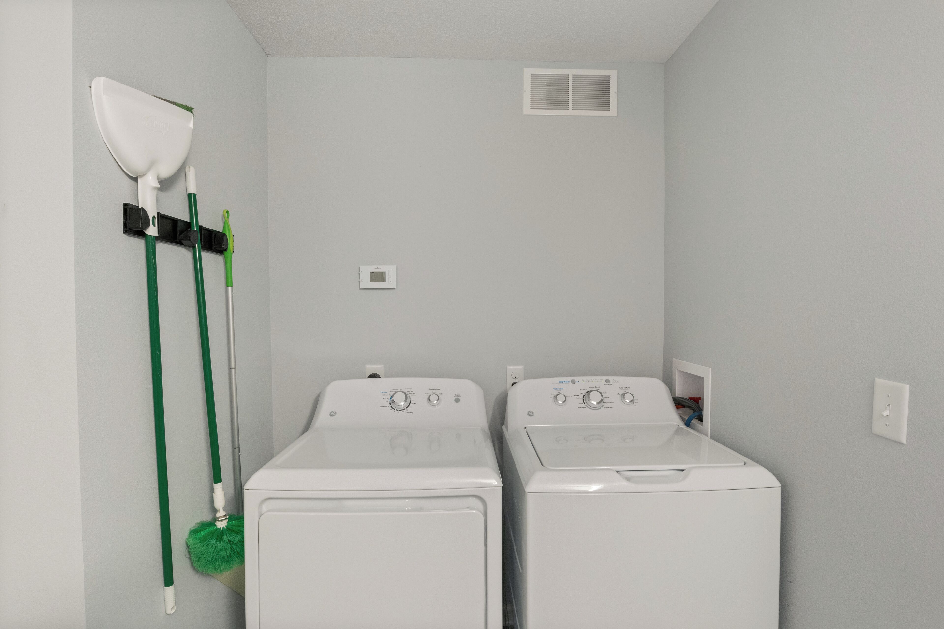A laundry room with two front-loading washing machines, a wall-mounted mirror, and a vent.