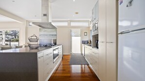 A modern kitchen with white cabinetry, a central island, and a view to the outside. - Spacious 3-bed Townhouse Near Dromana Beach (Melbourne)