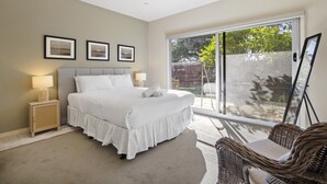 A bedroom with a large bed, a nightstand with a lamp, a wicker chair, and a sliding glass door to the outside. - Spacious 3-bed Townhouse Near Dromana Beach (Melbourne)