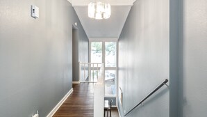 A modern interior with a wooden staircase, a chandelier, and a view to an outdoor balcony. - Our Cove Retreat - Perfect for Wave-free Swimming, Tanning & Prime Location Fun! (Lake Ozark)