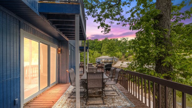 A deck with outdoor furniture, a railing, and a view of a house and trees. - Our Cove Retreat - Perfect for Wave-free Swimming, Tanning & Prime Location Fun! (Lake Ozark)