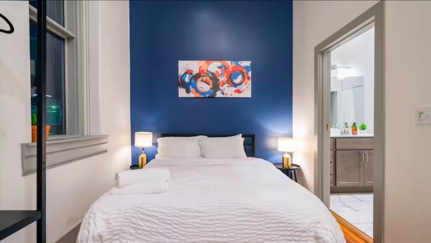 Een moderne hotelkamer met een groot bed, twee bedlampen, een blauwe accentmuur en een kleurrijk abstract schilderij.
