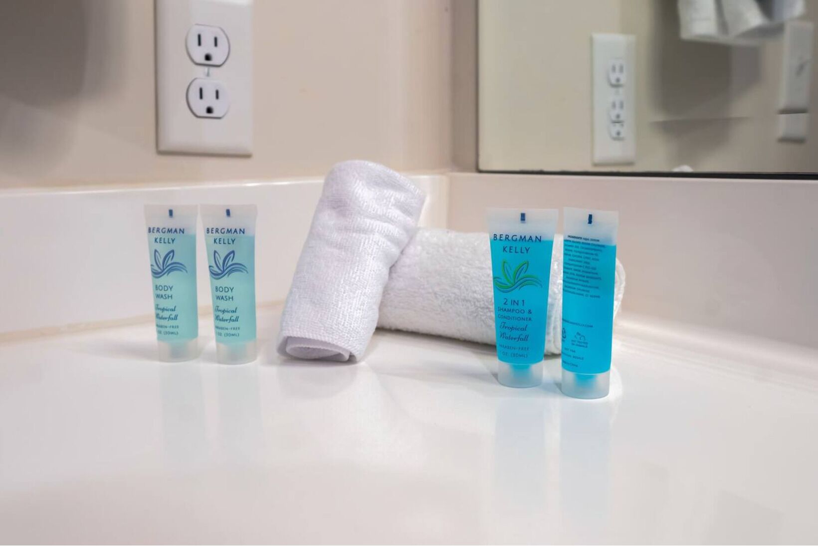 Un meuble-lavabo de salle de bain avec trois flacons de gel douche Bergman Kelly, une serviette blanche et un miroir.