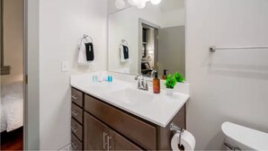 Een moderne badkamer met een witte wastafel, donkere houten kastjes, een grote spiegel en een toilet.