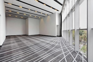 A spacious room with a patterned carpet, large windows, and a modern ceiling design.