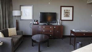 Ein Hotelzimmer mit einer Couch, einem Couchtisch, einem Fernseher auf einem Schrank, einer Lampe und gerahmten Bildern an der Wand.