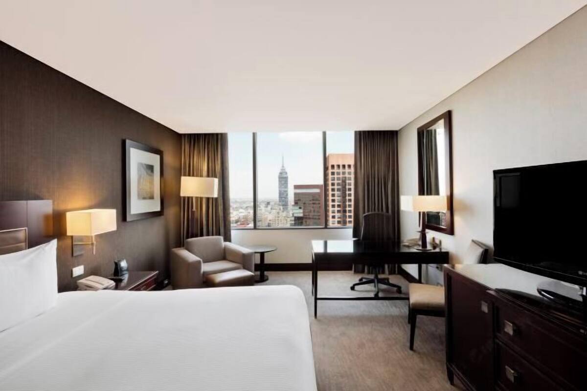 A hotel room with a bed, desk, chair, TV, and a city view.