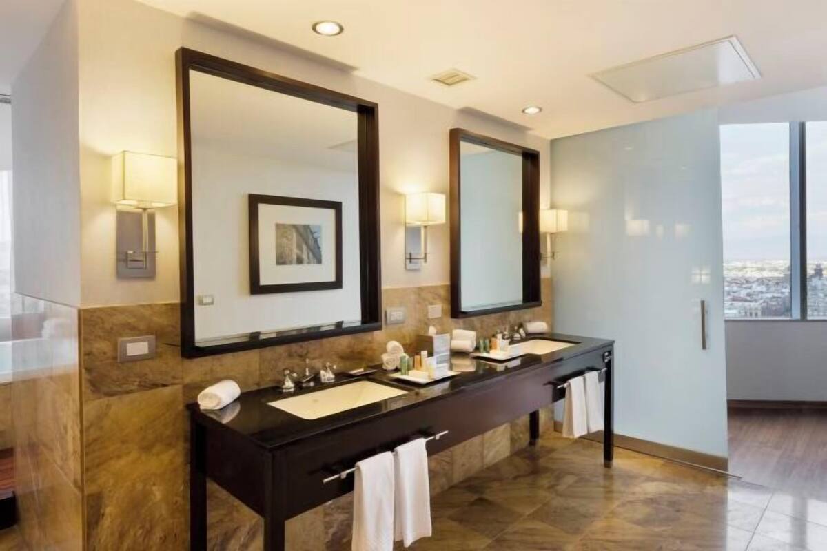 A modern bathroom with two sinks, large mirrors, and a city view.