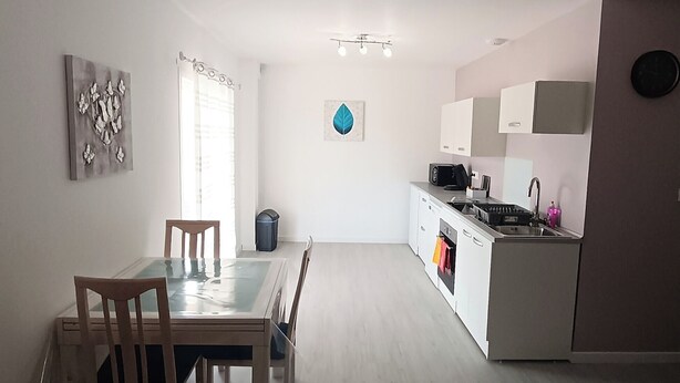 A modern kitchen with white cabinets and a built-in oven. There is a dining area with a wooden table and chairs. - Apartment in the immediate vicinity of Château de Maintenon (Pierres)