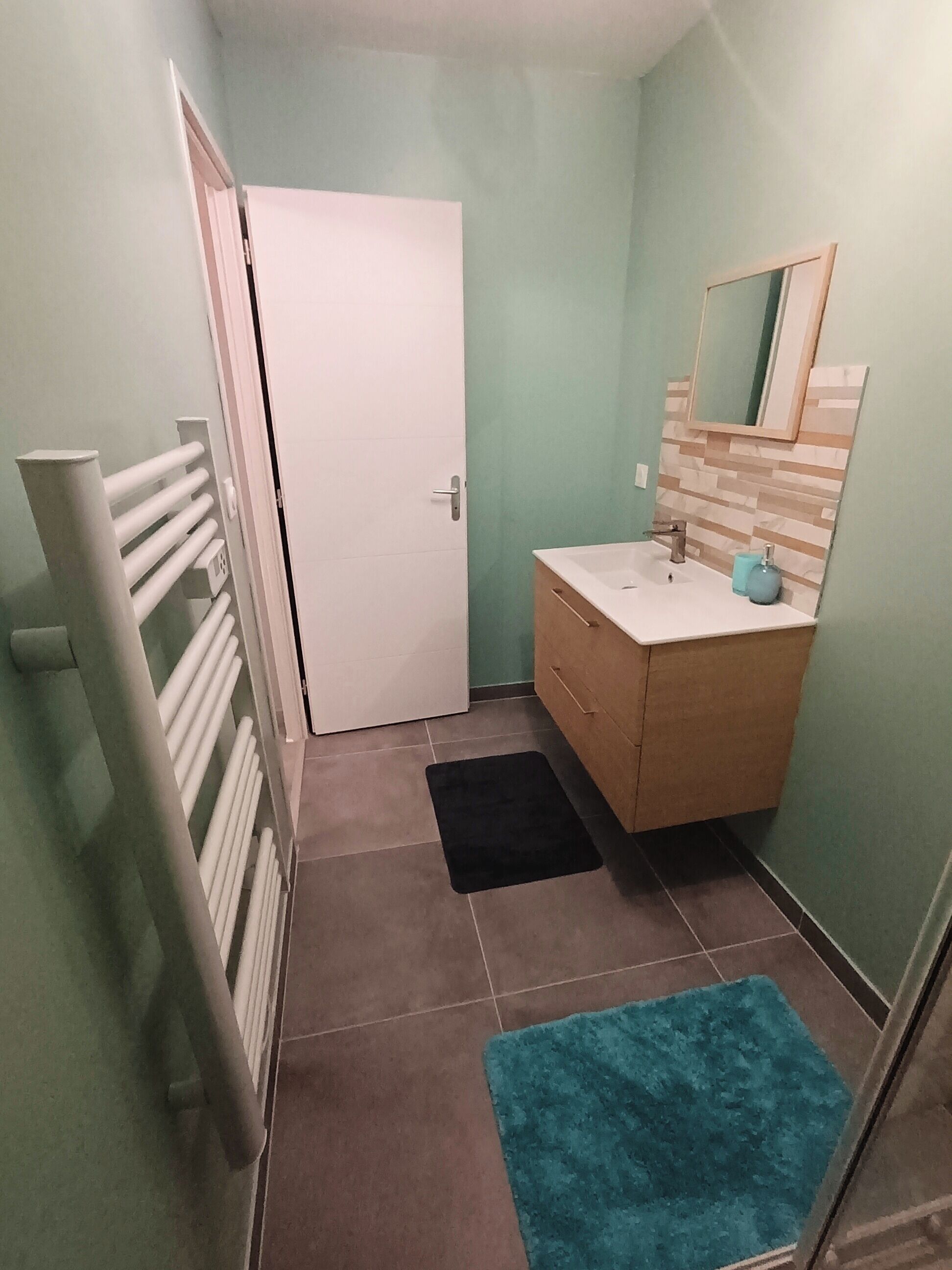 Ein kleines Badezimmer mit einer weißen Tür, einem Holzauszug, einem Spiegel und einem blauen Teppich.
