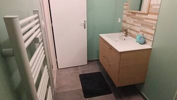 Ein kleines Badezimmer mit einer weißen Tür, einem Holzauszug, einem Spiegel und einem blauen Teppich.