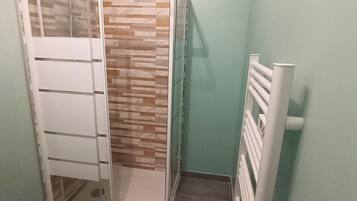 A bathroom with a shower enclosure, a towel rack, and a blue rug on the floor.