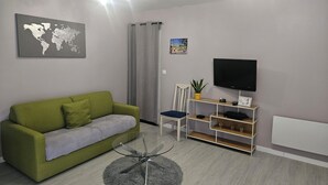 A modern living room with a green sofa, a glass coffee table, a flat-screen TV, and a world map artwork. - Apartment in the immediate vicinity of Château de Maintenon (Pierres)