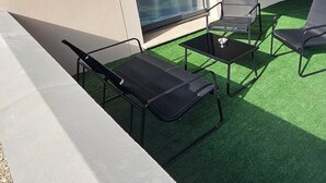 An outdoor seating area with a glass door, artificial grass, and a concrete floor. - Apartment in the immediate vicinity of Château de Maintenon (Pierres)
