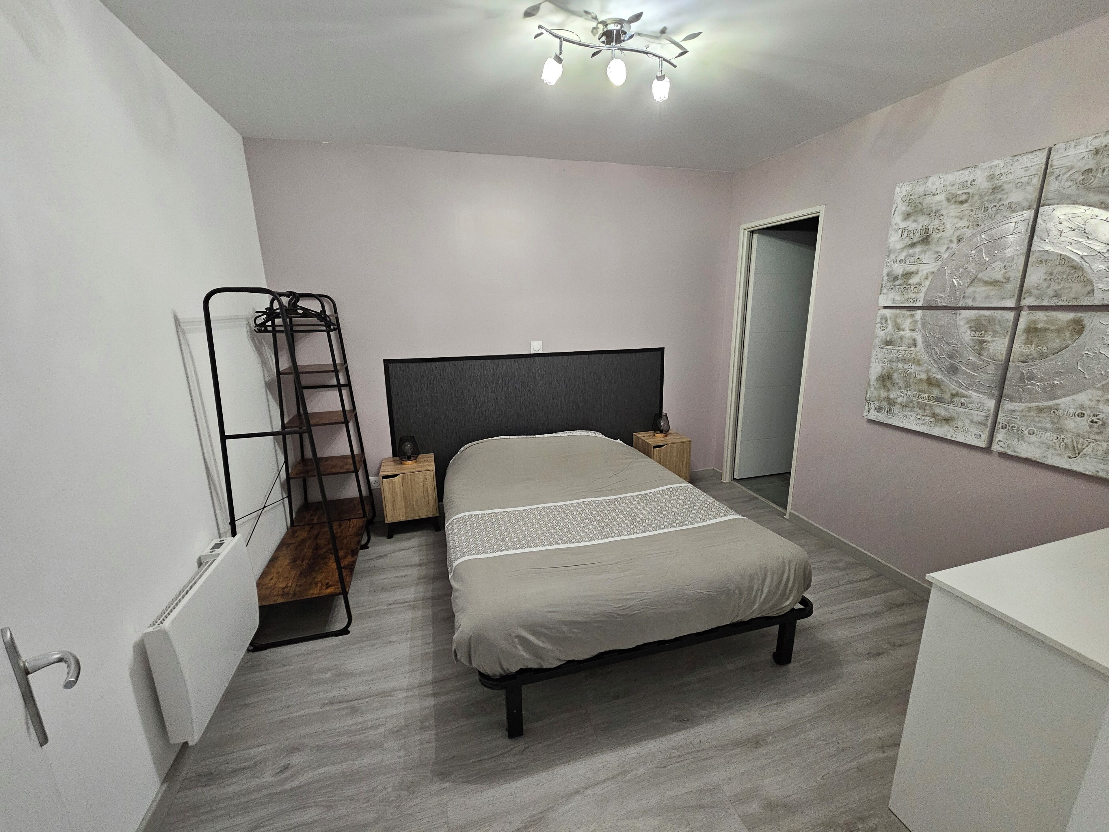 A bedroom with a bed, a ladder, a bedside table, a speaker, and a wall with artwork.