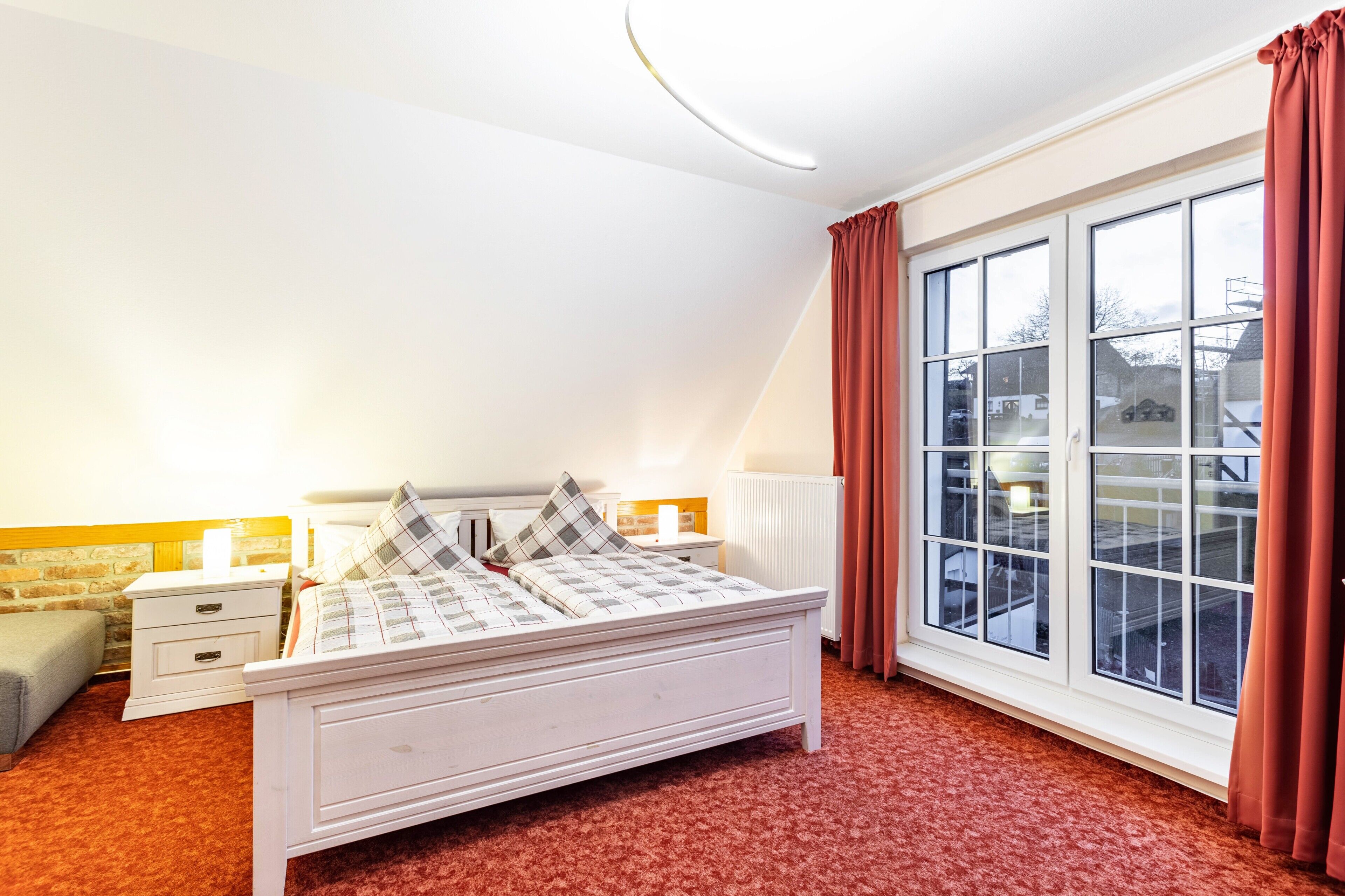 Ein Schlafzimmer mit Bett, Nachttischen, einem Fenster und Blick nach draußen.