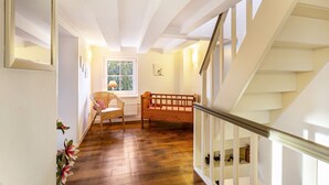 A staircase with white railings, a wooden floor, a wicker chair, a wooden crib, and a window with a view of greenery.