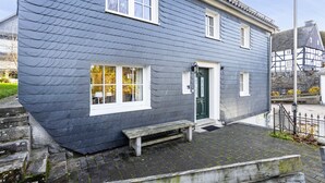 A two-story building with a dark blue exterior, white trim around windows and doors, a small front porch with a bench, and a stone staircase leading up to the entrance.