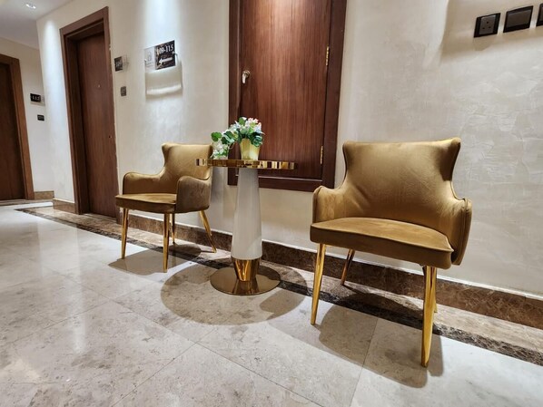 A hallway with two gold-colored chairs and a white pedestal table with a vase of flowers.