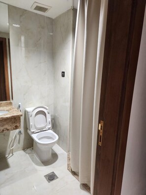Un bagno con WC, pareti in marmo, lavandino e tenda per la doccia.